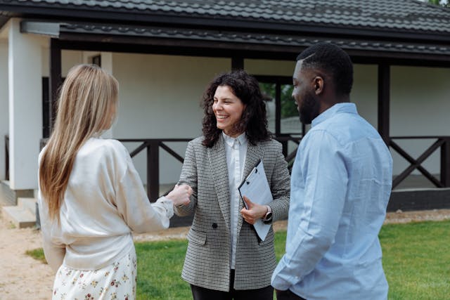 Two people shaking hands outside while one holds a clipboard and another person stands near them